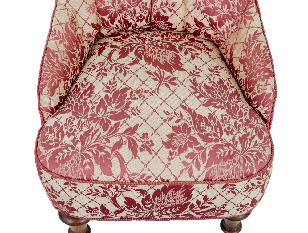 An early 20th century three-piece upholstered salon suite featuring a two-seater settee and two matching armchairs with pink and cream floral damask pattern, button-tufted fluted backs, and turned wooden legs with brass castors. View X