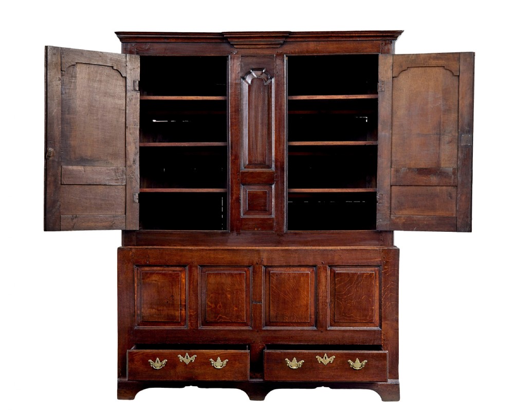 An 18th-century dark oak housekeepers cupboard featuring arched fielded panel doors above a lower section fitted with drawers and brass handles. View II