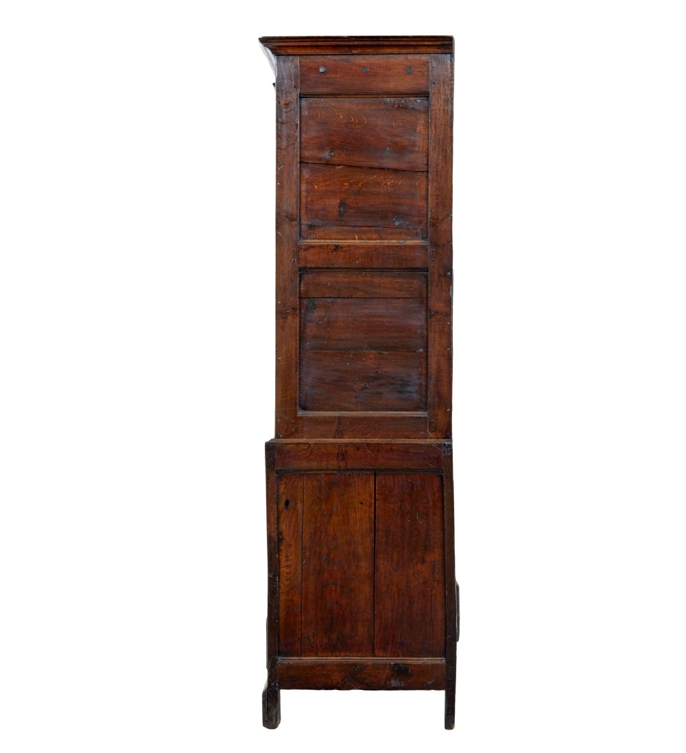 An 18th-century dark oak housekeepers cupboard featuring arched fielded panel doors above a lower section fitted with drawers and brass handles. View V