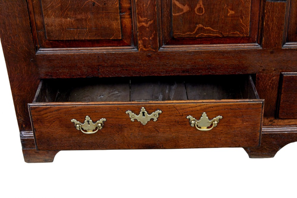 An 18th-century dark oak housekeepers cupboard featuring arched fielded panel doors above a lower section fitted with drawers and brass handles. View VI
