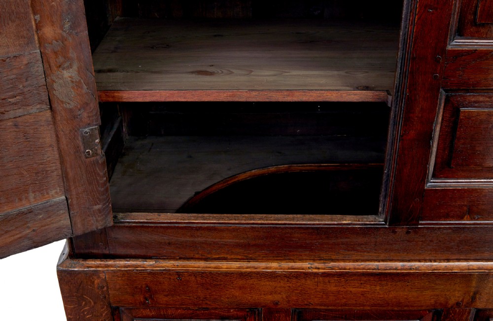 An 18th-century dark oak housekeepers cupboard featuring arched fielded panel doors above a lower section fitted with drawers and brass handles. View VII