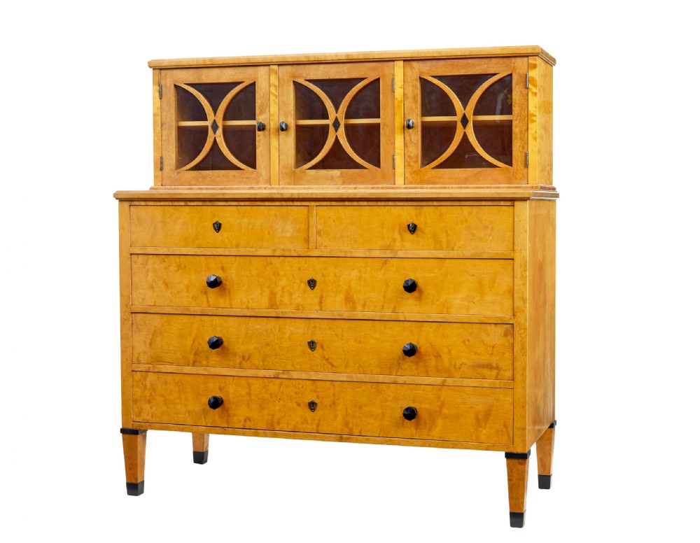 A late 19th-century Swedish satin birch cabinet featuring a three-door glazed top section with curved glazing bars resting on a five-drawer chest with dark faceted knobs.