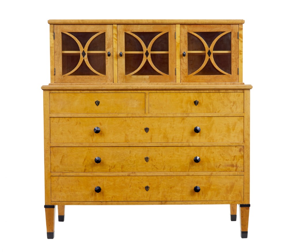 A late 19th-century Swedish satin birch cabinet featuring a three-door glazed top section with curved glazing bars resting on a five-drawer chest with dark faceted knobs. View II