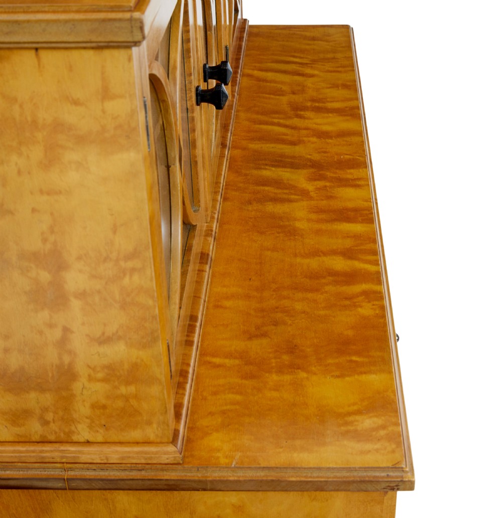A late 19th-century Swedish satin birch cabinet featuring a three-door glazed top section with curved glazing bars resting on a five-drawer chest with dark faceted knobs. View VIII