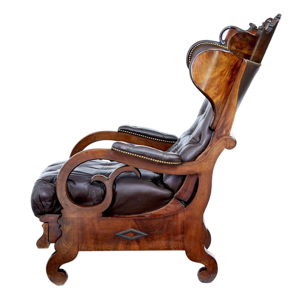 A mid-19th-century French reclining armchair featuring carved mahogany scrolled arms, a cresting motif, and deep-buttoned dark brown leather upholstery trimmed with brass studs. View VI
