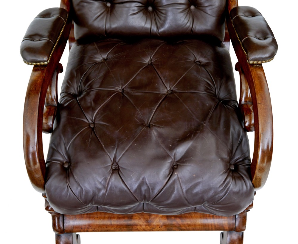 A mid-19th-century French reclining armchair featuring carved mahogany scrolled arms, a cresting motif, and deep-buttoned dark brown leather upholstery trimmed with brass studs. View IX
