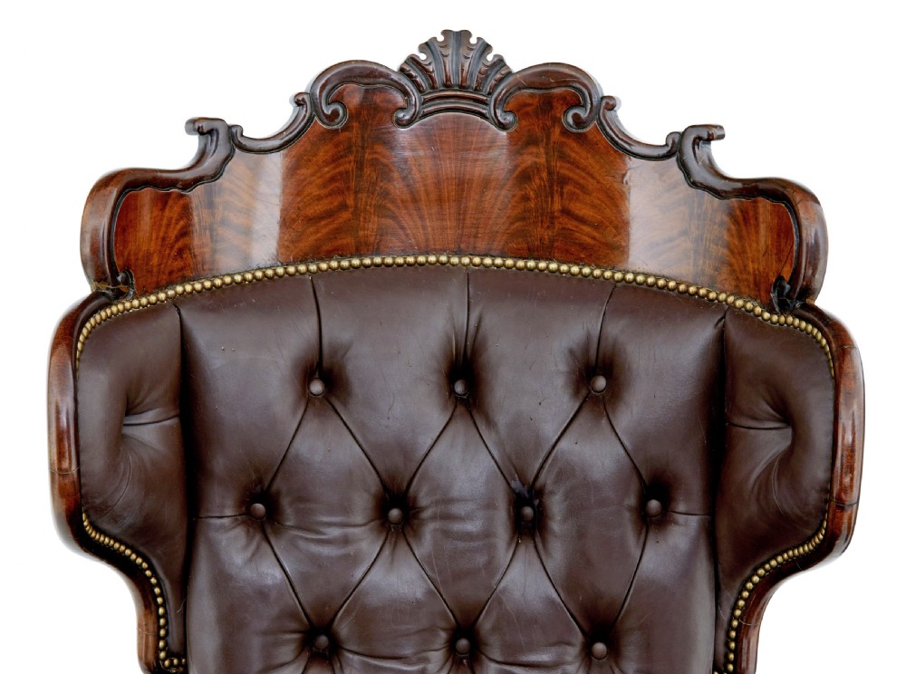 A mid-19th-century French reclining armchair featuring carved mahogany scrolled arms, a cresting motif, and deep-buttoned dark brown leather upholstery trimmed with brass studs. View X