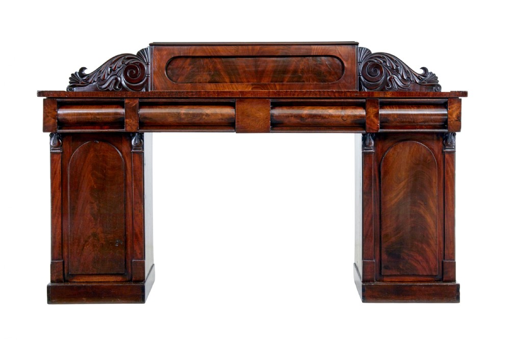 A nineteenth-century William IV mahogany pedestal sideboard featuring an architectural splashback with carved scrolls, frieze section, and two cupboard pedestals on plinth bases.