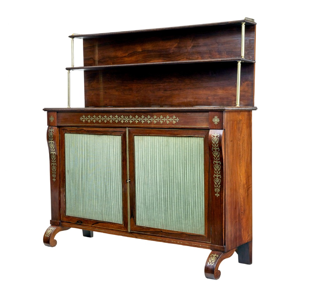 A 19th-century Regency palisander chiffonier with brass inlay, a two-tier raised shelf back supported by brass columns, and green pleated fabric door panels.