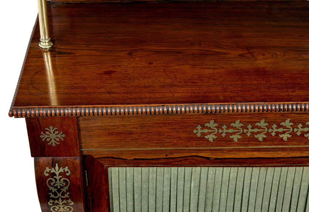 A 19th-century Regency palisander chiffonier with brass inlay, a two-tier raised shelf back supported by brass columns, and green pleated fabric door panels. View IX