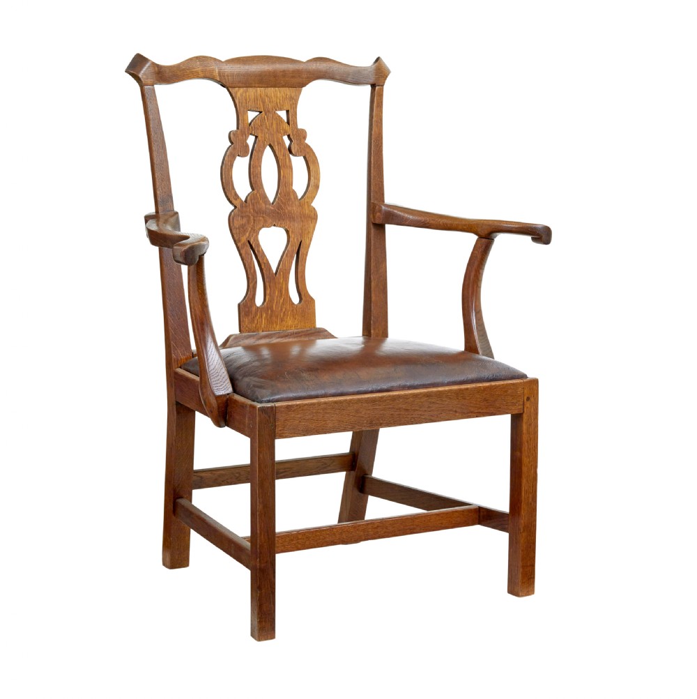 A 19th-century solid oak armchair featuring shepherds crook armrests, a carved pierced back splat, and a brown leather seat cushion.