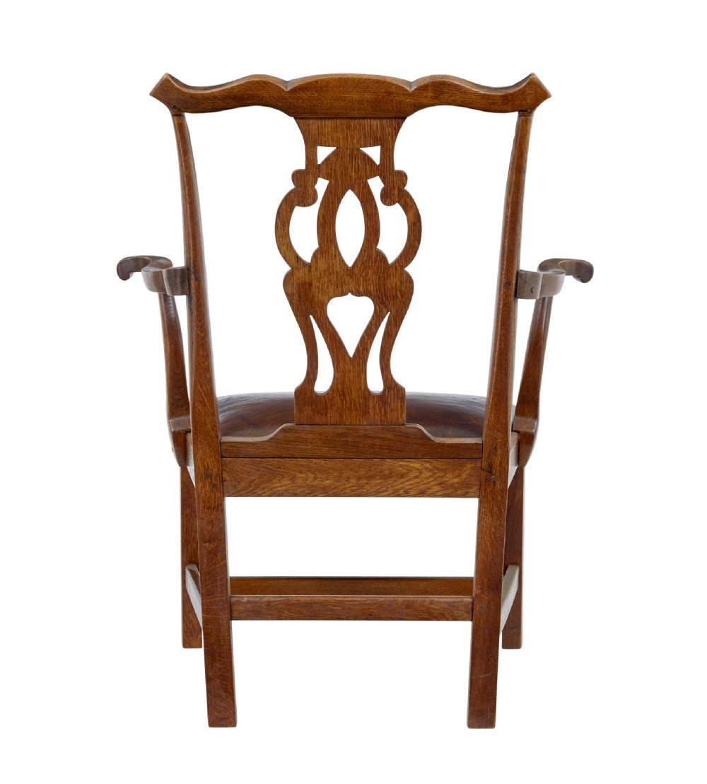 A 19th-century solid oak armchair featuring shepherds crook armrests, a carved pierced back splat, and a brown leather seat cushion. View V