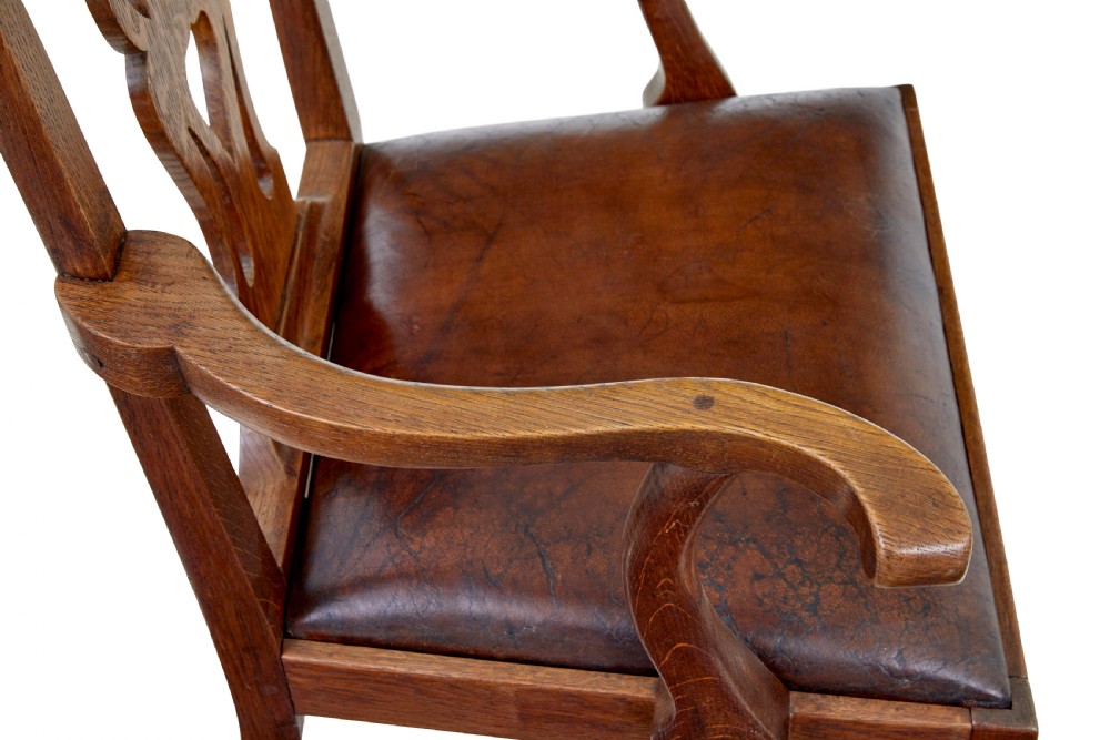 A 19th-century solid oak armchair featuring shepherds crook armrests, a carved pierced back splat, and a brown leather seat cushion. View VI