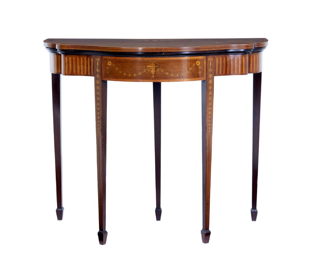 A 19th-century Sheraton Revival mahogany card table featuring a demi-lune fold-over top, satinwood marquetry with urn and swag motifs, and four tapered square legs.