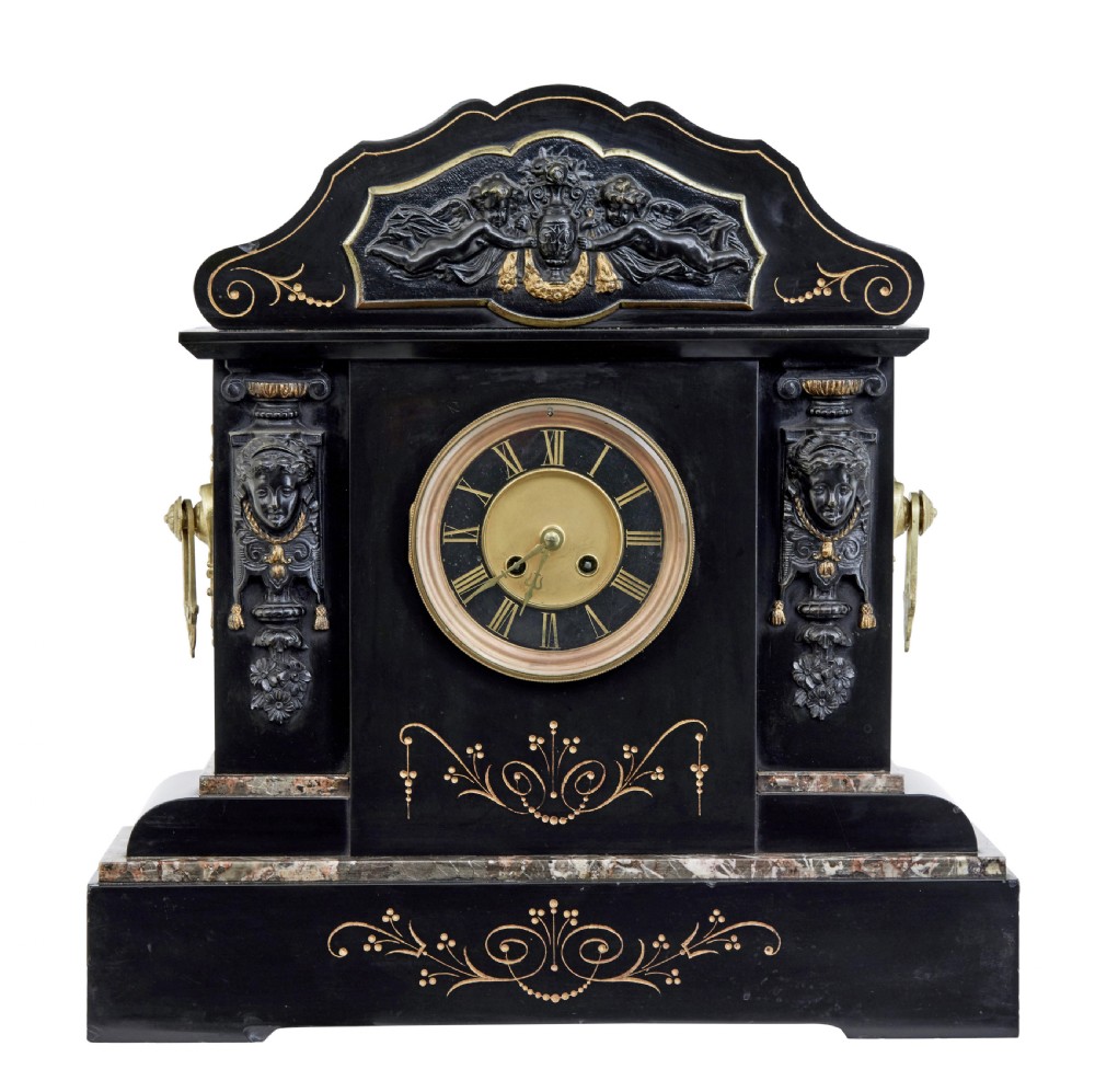 A High Victorian black marble mantel clock featuring gold incised scrollwork, a classical cherub relief panel, and a central circular dial with Roman numerals.