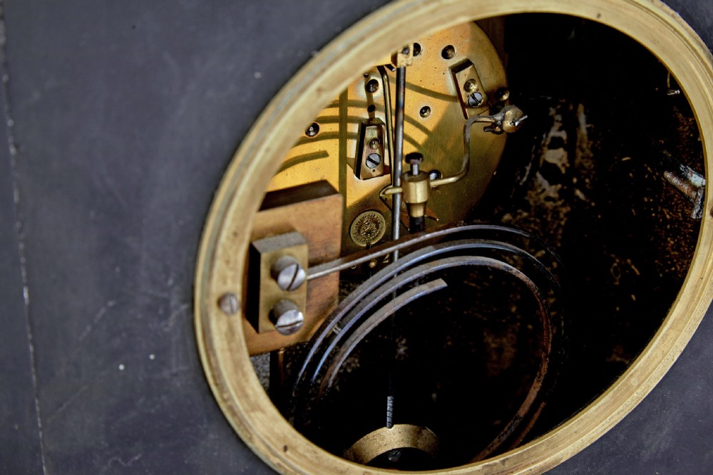 A High Victorian black marble mantel clock featuring gold incised scrollwork, a classical cherub relief panel, and a central circular dial with Roman numerals. View VI