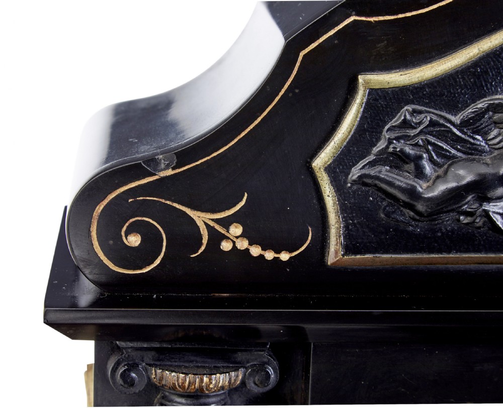 A High Victorian black marble mantel clock featuring gold incised scrollwork, a classical cherub relief panel, and a central circular dial with Roman numerals. View VII