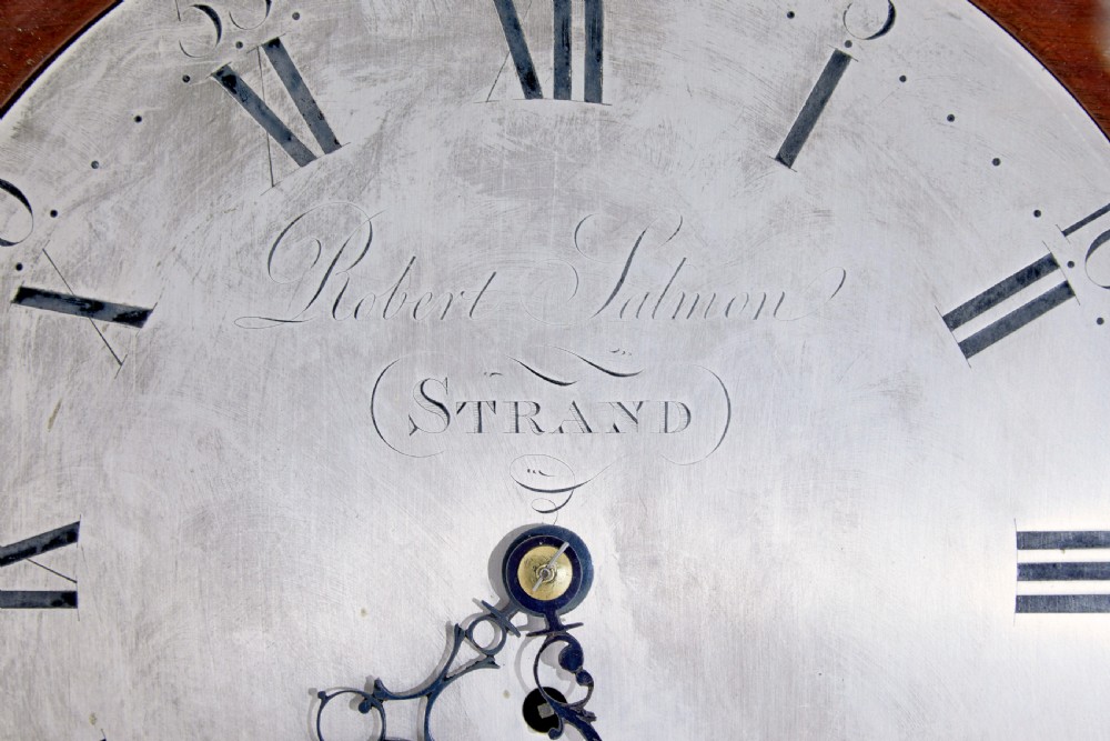 An 18th-century Georgian wall clock featuring an engraved silvered dial with Roman numerals, a brass bezel, and a circular mahogany surround. View IV
