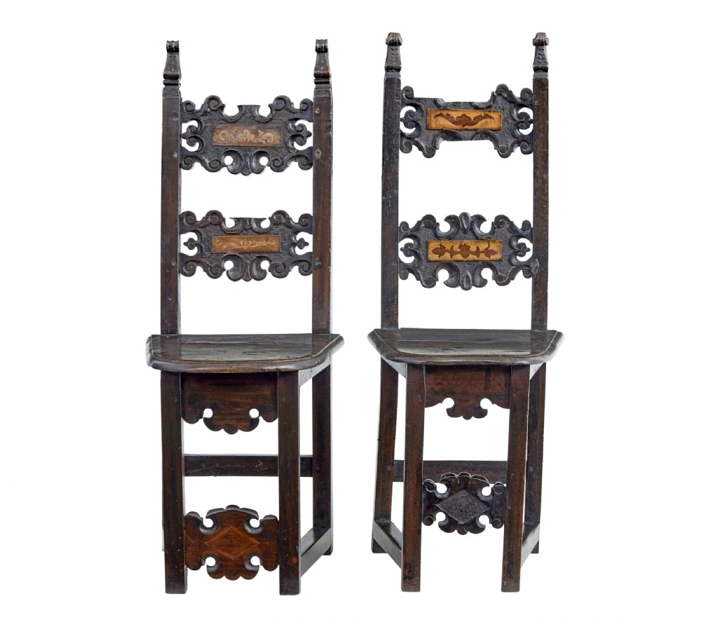 A pair of 19th-century dark oak Carolean-inspired hall chairs featuring intricate scrollwork carving, inlaid back panels, and turned finials.