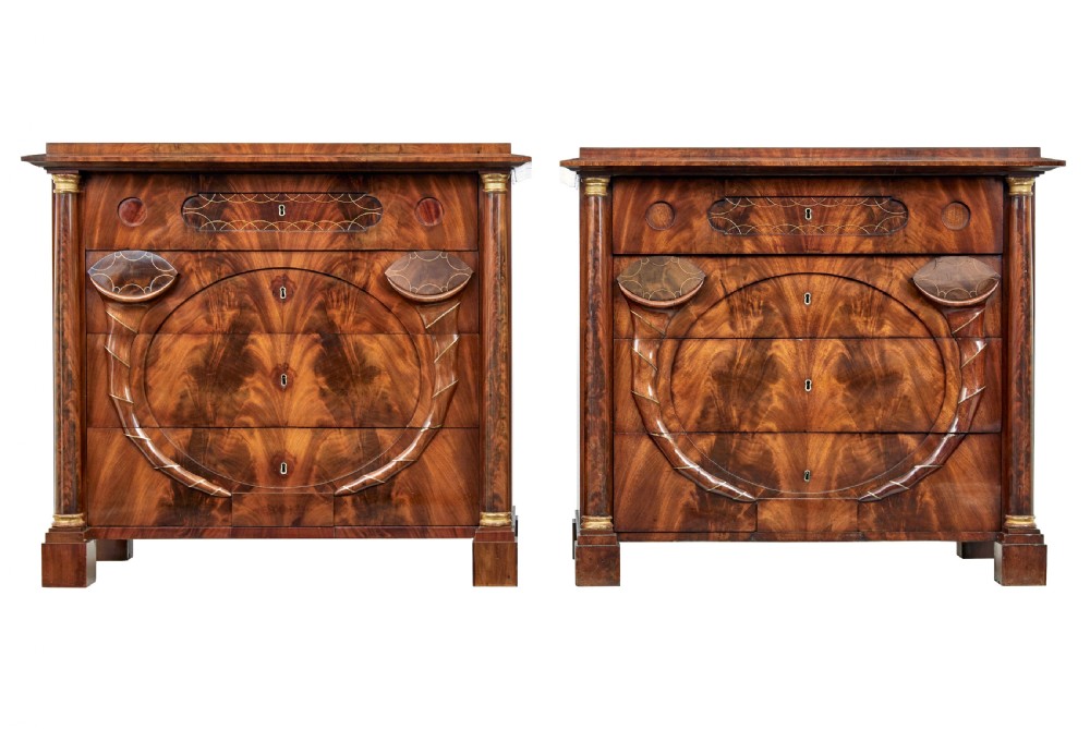 A matching pair of early nineteenth-century mahogany Biedermeier commodes featuring carved cornucopia motifs and side columns.