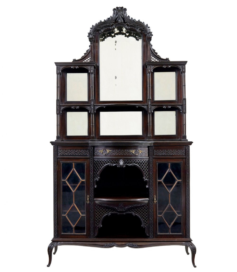 An Edwardian Chippendale Revival dark mahogany display cabinet featuring a multi-paneled mirrored upper section, carved crest, fretwork, and glazed side doors on cabriole legs.