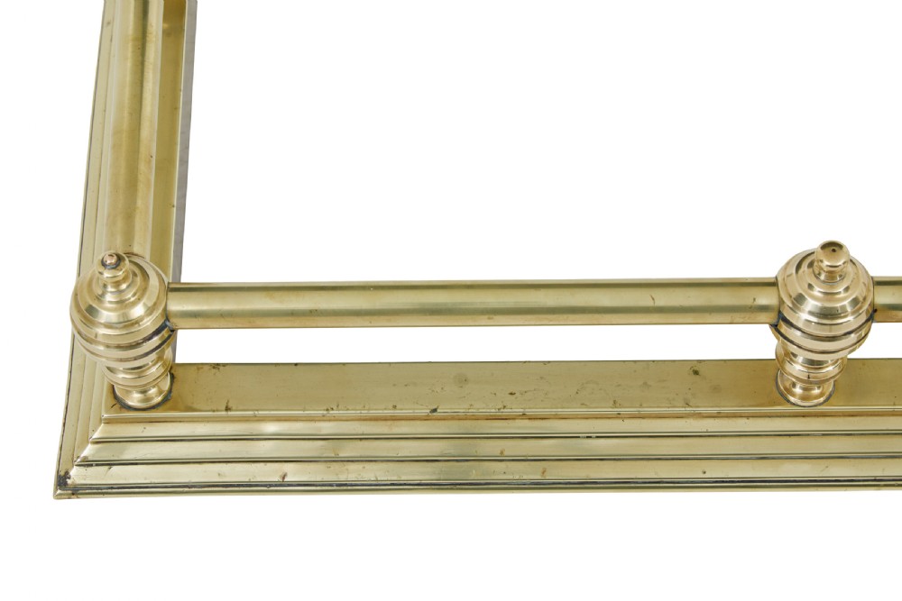 An early 20th-century polished brass fireside fender featuring a stepped base and a raised top rail supported by turned spherical finials. View III