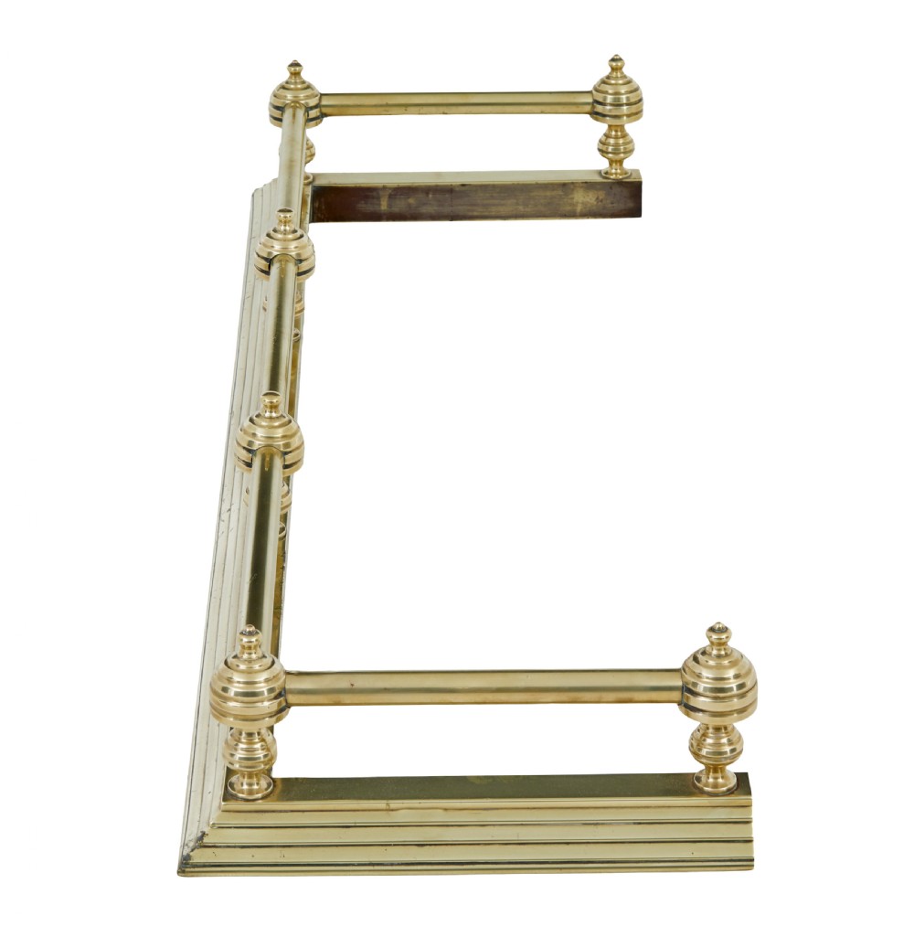 An early 20th-century polished brass fireside fender featuring a stepped base and a raised top rail supported by turned spherical finials. View V