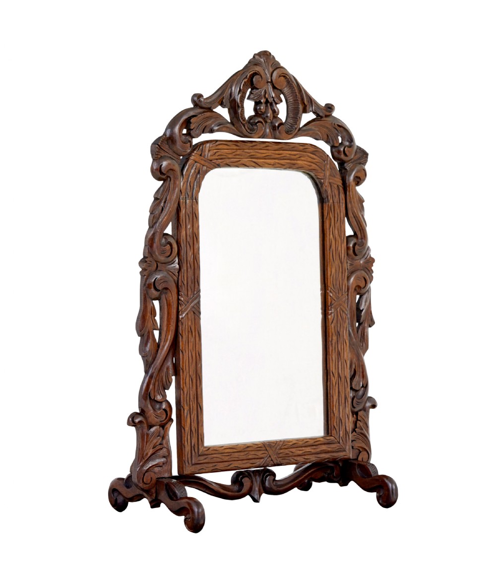 A late 19th-century dark oak tabletop vanity mirror featuring elaborate Rococo Revival scrollwork and an arched frame.
