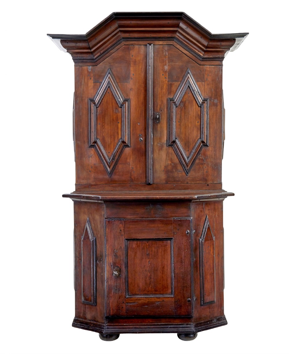 An 18th-century Scandinavian pine Baroque cupboard featuring faceted sides, geometric diamond mouldings on the upper doors, and a projected corniced top.