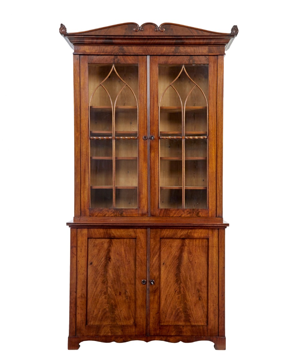 An early 19th-century flame mahogany bookcase featuring a pediment top, two upper glazed doors with arched astragal glazing, and a double-door cupboard base.