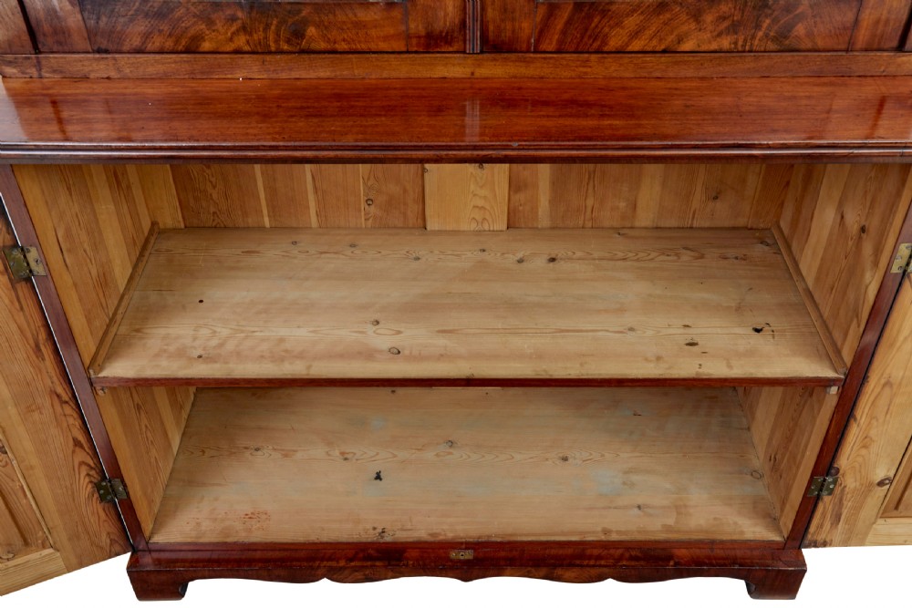 An early 19th-century flame mahogany bookcase featuring a pediment top, two upper glazed doors with arched astragal glazing, and a double-door cupboard base. View VIII