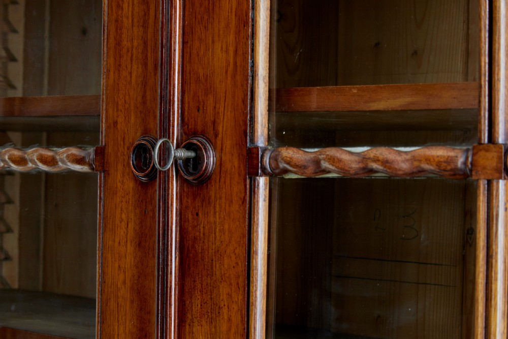 An early 19th-century flame mahogany bookcase featuring a pediment top, two upper glazed doors with arched astragal glazing, and a double-door cupboard base. View X