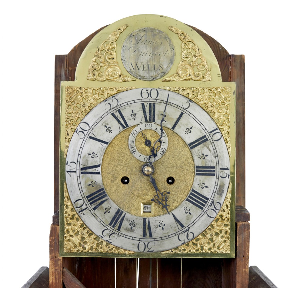 An 18th-century oak longcase clock featuring a brass dial, pediment hood with brass finials, rectangular trunk door, and plinth base. View VII