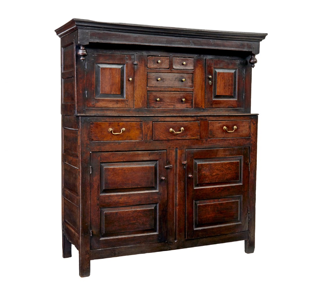 A seventeenth-century dark oak Welsh court cupboard featuring raised geometric panels, turned pendant drops, small central drawers, and double lower doors.