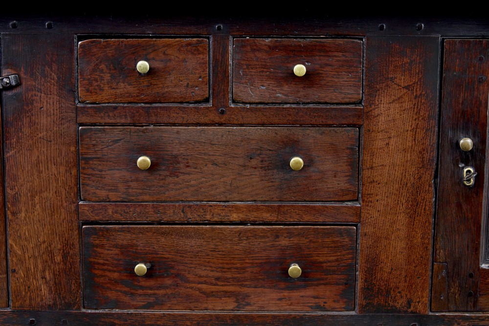 A seventeenth-century dark oak Welsh court cupboard featuring raised geometric panels, turned pendant drops, small central drawers, and double lower doors. View II