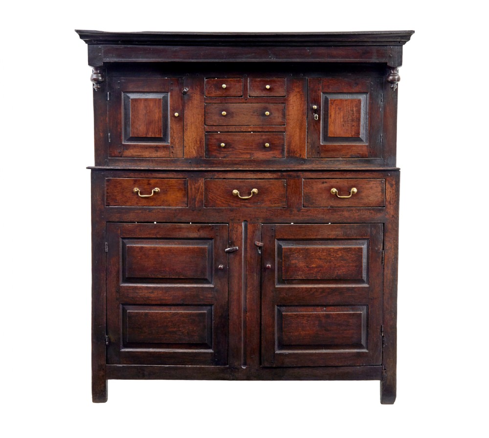 A seventeenth-century dark oak Welsh court cupboard featuring raised geometric panels, turned pendant drops, small central drawers, and double lower doors. View V