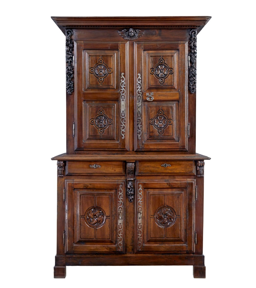 An eighteenth-century French carved walnut cupboard in two tiers featuring geometric relief panels, floral motifs, cherub carvings, and decorative steel hinges.