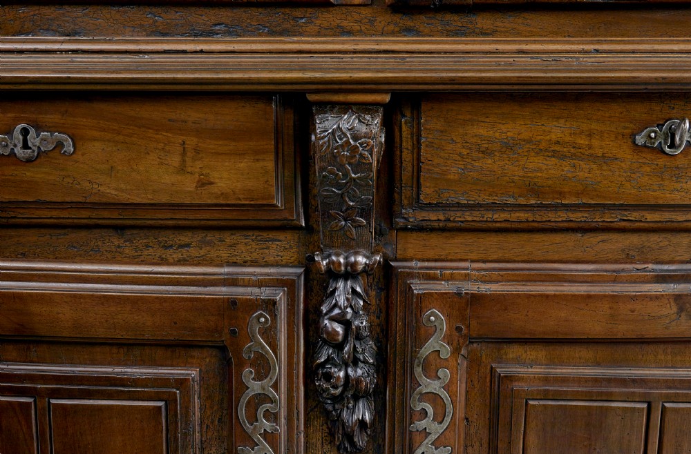 An eighteenth-century French carved walnut cupboard in two tiers featuring geometric relief panels, floral motifs, cherub carvings, and decorative steel hinges. View VII