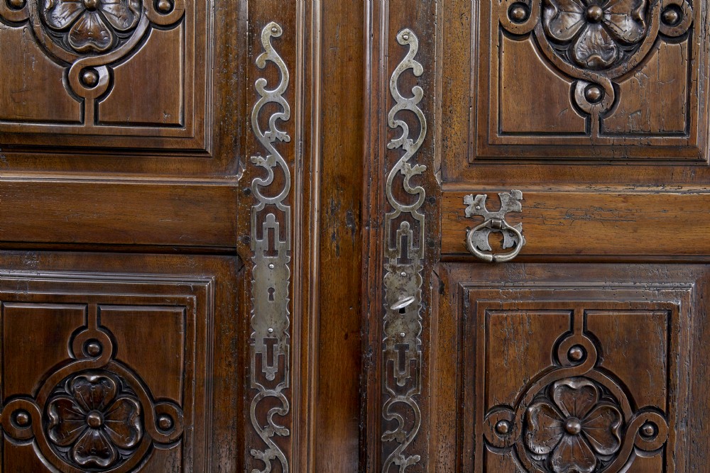 An eighteenth-century French carved walnut cupboard in two tiers featuring geometric relief panels, floral motifs, cherub carvings, and decorative steel hinges. View VIII