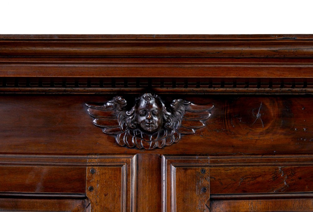 An eighteenth-century French carved walnut cupboard in two tiers featuring geometric relief panels, floral motifs, cherub carvings, and decorative steel hinges. View X
