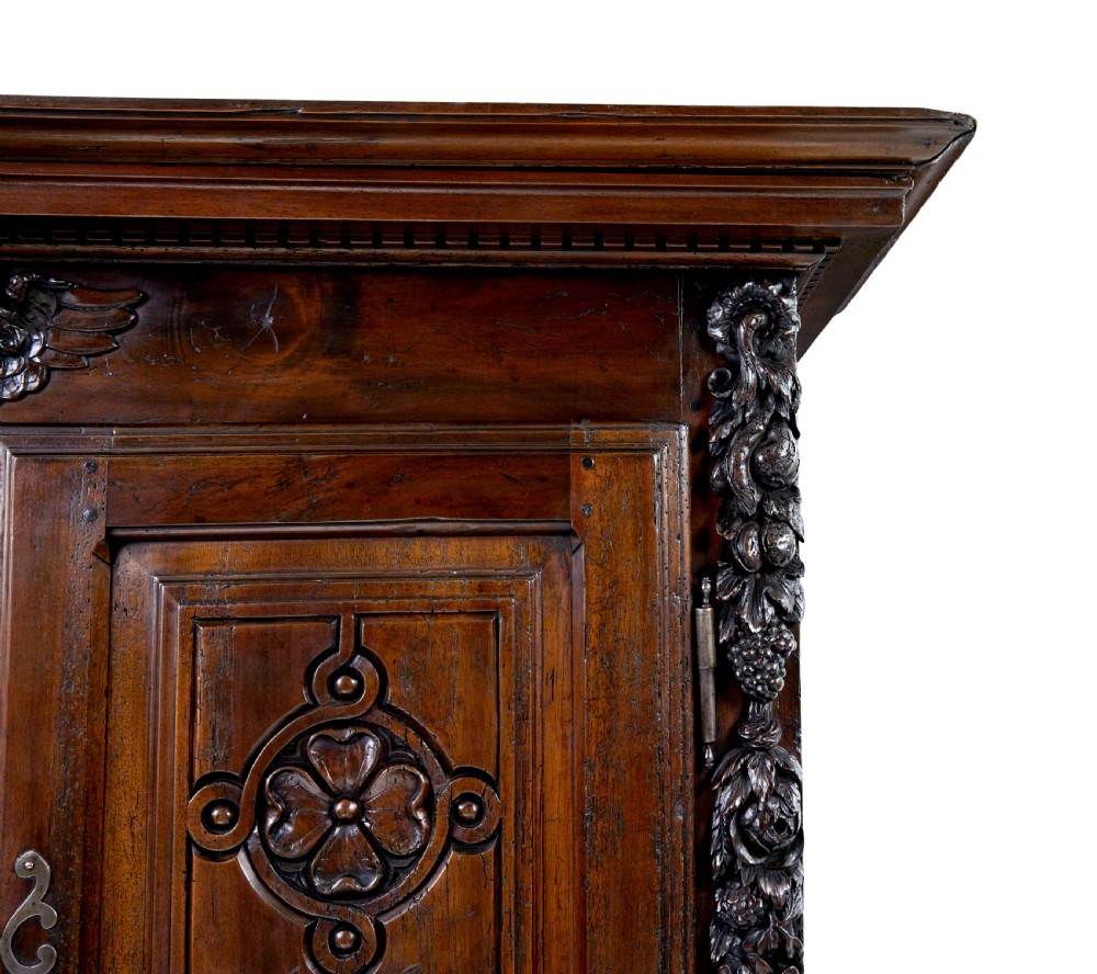An eighteenth-century French carved walnut cupboard in two tiers featuring geometric relief panels, floral motifs, cherub carvings, and decorative steel hinges. View XI