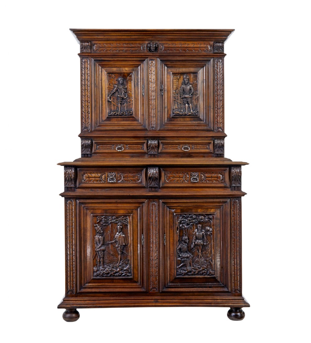 Mid 19th century dark walnut two-tiered Italian cabinet featuring intricately carved relief panels of figures, decorative drawers, and bun feet.
