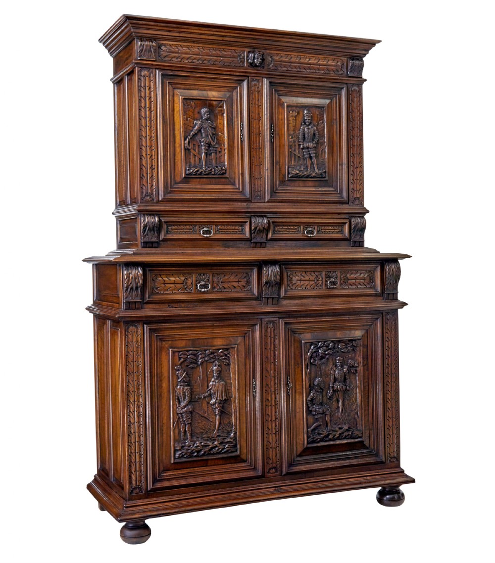 Mid 19th century dark walnut two-tiered Italian cabinet featuring intricately carved relief panels of figures, decorative drawers, and bun feet. View II