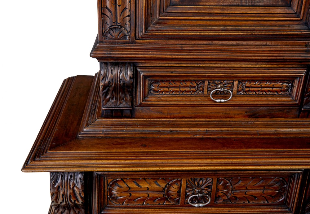 Mid 19th century dark walnut two-tiered Italian cabinet featuring intricately carved relief panels of figures, decorative drawers, and bun feet. View VIII