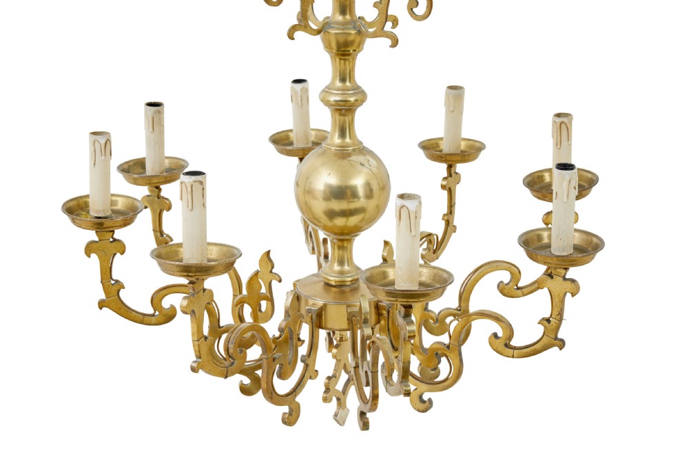An early 20th century brass eight-arm chandelier featuring scrolling branches, circular drip pans, candle sleeves, a central baluster stem, and a suspension chain. View II