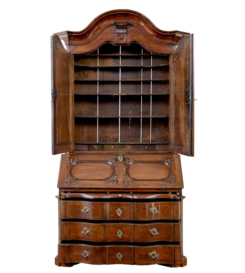 An 18th-century Norwegian carved oak bureau bookcase featuring an arched pediment, panelled upper doors, a slant-front writing slant, serpentine lower drawers, and brass escutcheons. View III