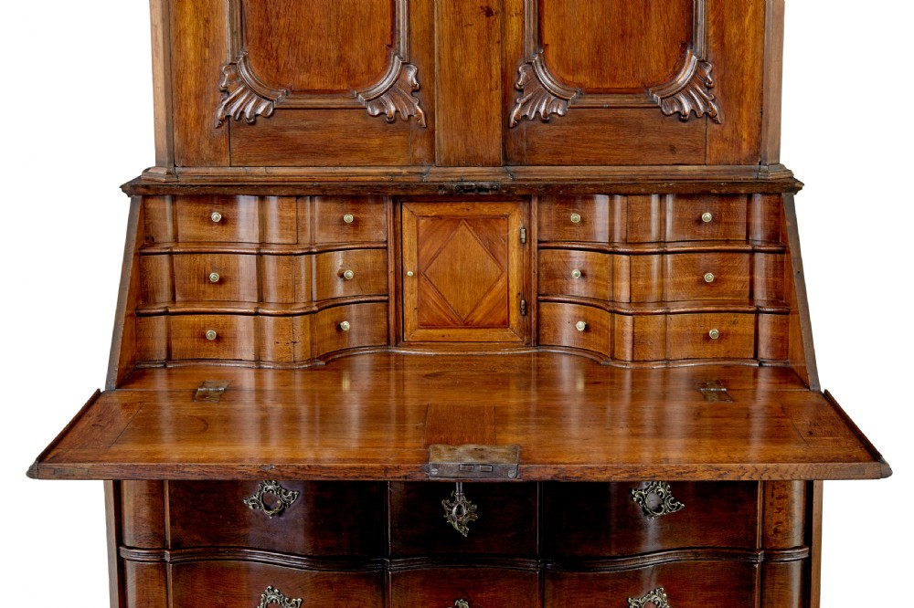 An 18th-century Norwegian carved oak bureau bookcase featuring an arched pediment, panelled upper doors, a slant-front writing slant, serpentine lower drawers, and brass escutcheons. View IV