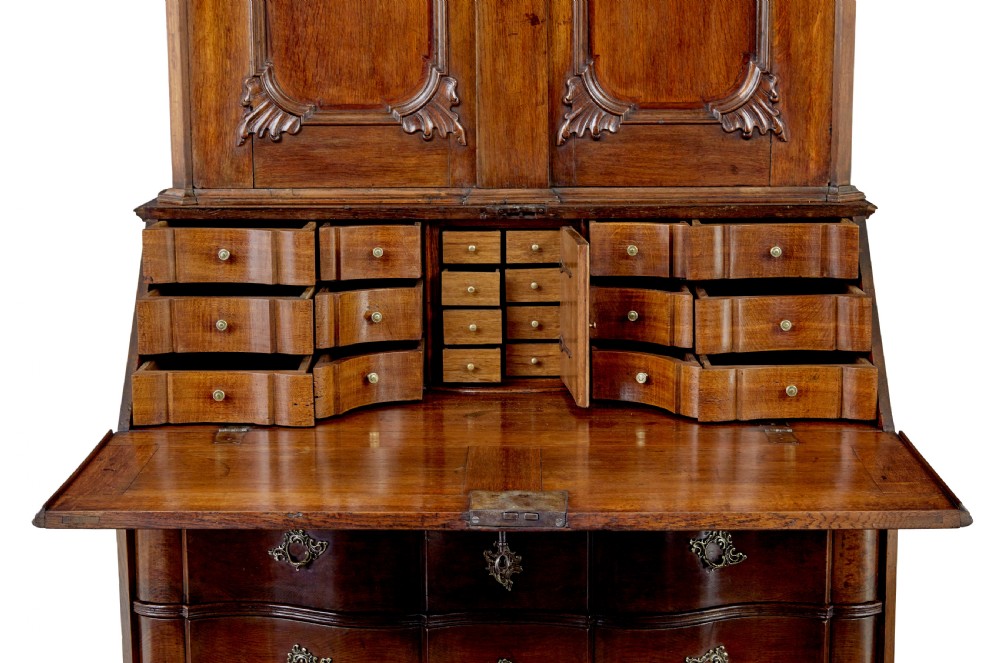 An 18th-century Norwegian carved oak bureau bookcase featuring an arched pediment, panelled upper doors, a slant-front writing slant, serpentine lower drawers, and brass escutcheons. View V