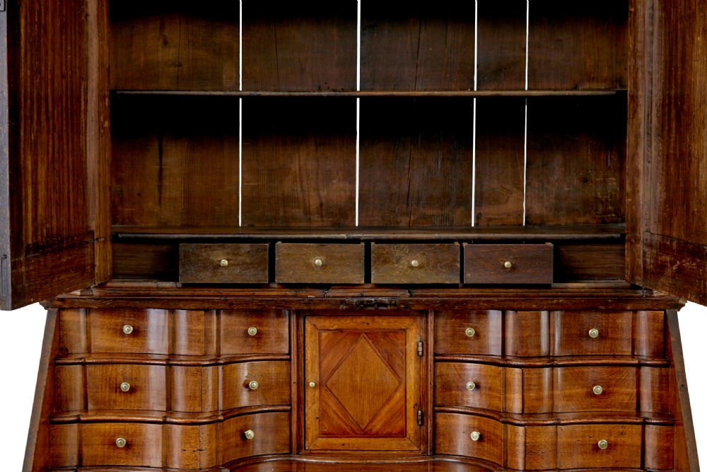 An 18th-century Norwegian carved oak bureau bookcase featuring an arched pediment, panelled upper doors, a slant-front writing slant, serpentine lower drawers, and brass escutcheons. View VI