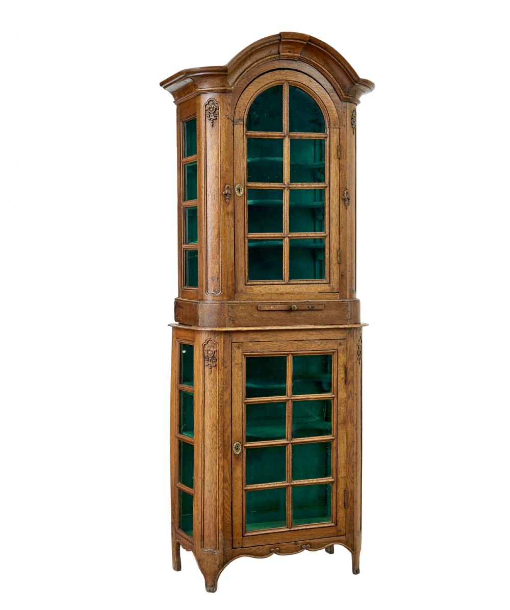 A mid-19th-century carved oak display cabinet featuring glazed doors, arched pediment, and green fabric interior lining.